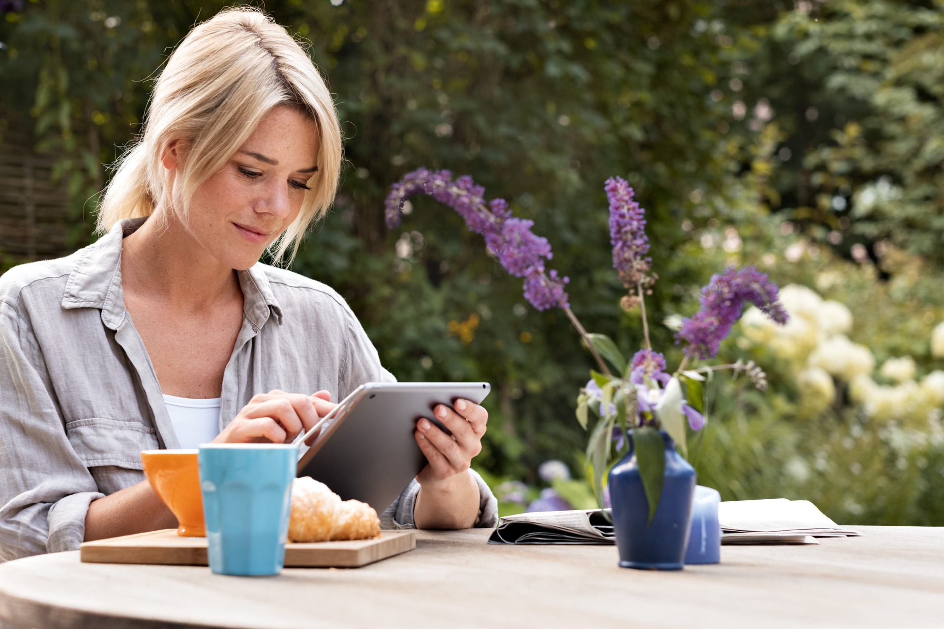 Uma mulher usando um tablet à mesa de almoço no jardim