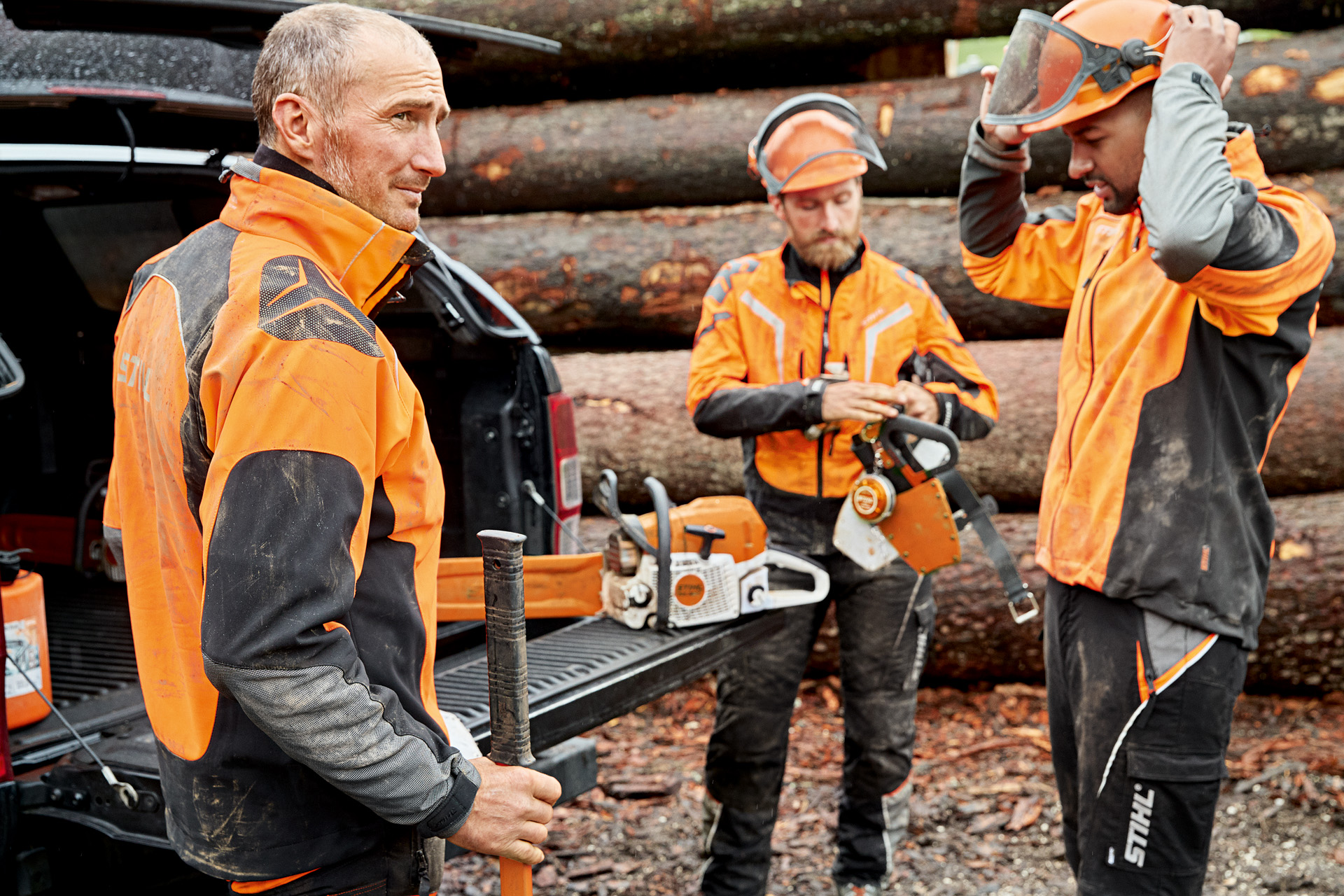 Três trabalhadores florestais com equipamento de proteção individual em frente a um pedaço de madeira na floresta.